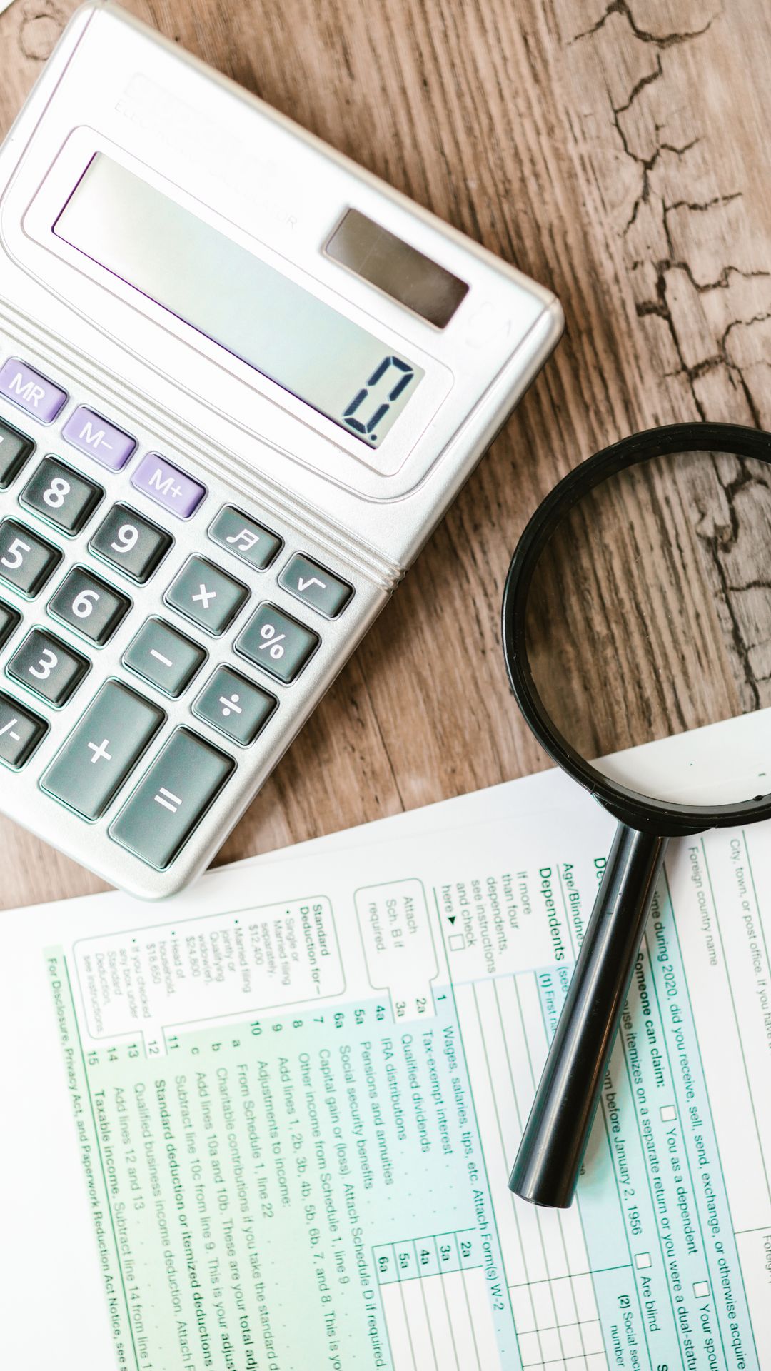 Calculatrice grise et loupe posées sur un formulaire fiscal, sur une table en bois