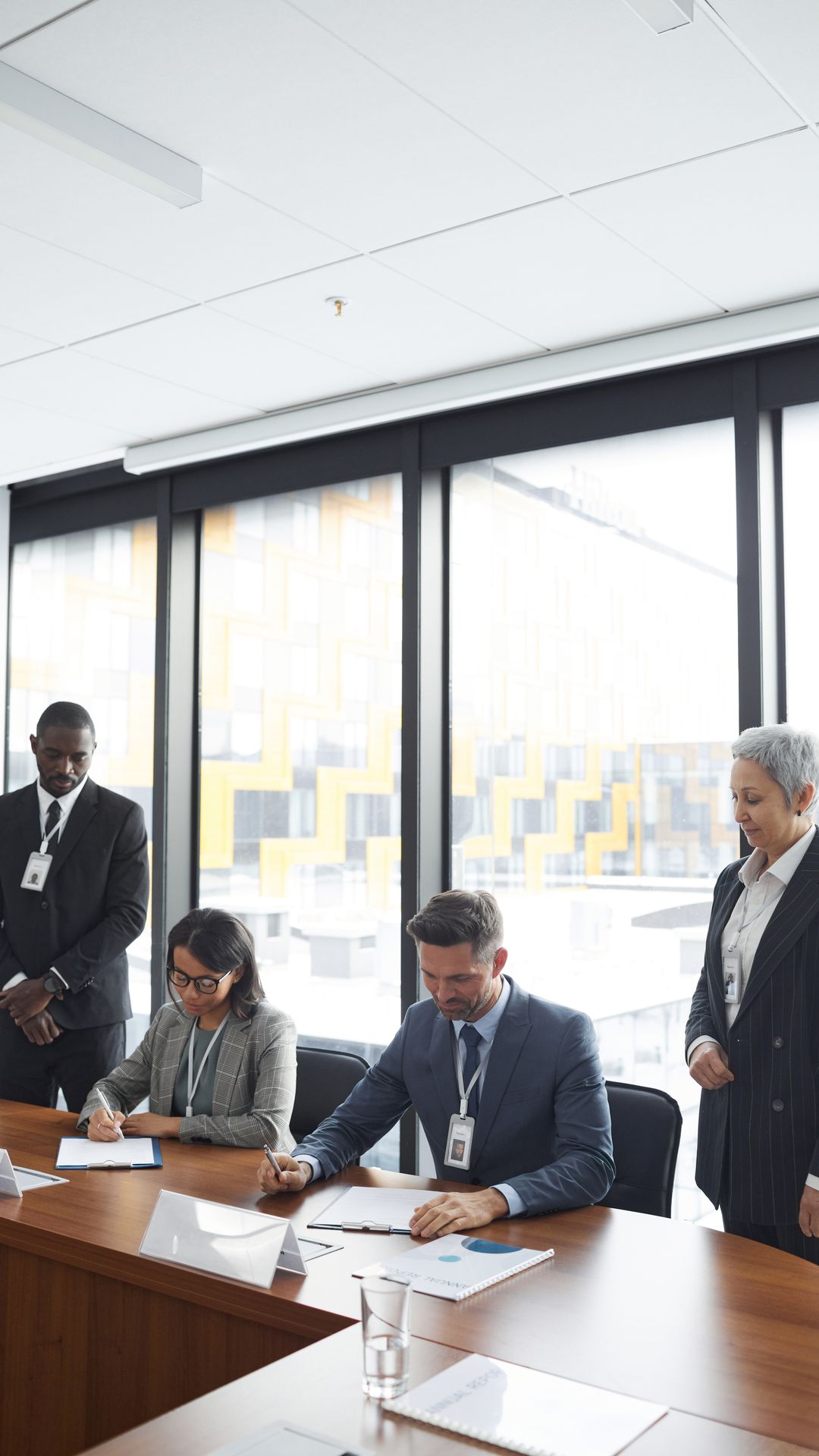 Réunion de signature autour d'une table en bois : deux personnes assises signent, deux autres restent debout
