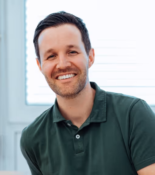 Smiling man with short dark hair wearing a green polo shirt in a bright indoor setting.