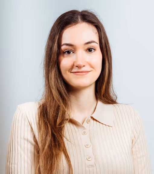 Smiling woman with long brown hair wearing a beige ribbed buttoned shirt against a light background.