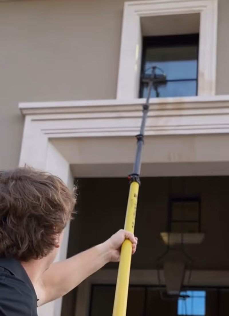 Technician cleaning an upper-storey window with a water-fed pole