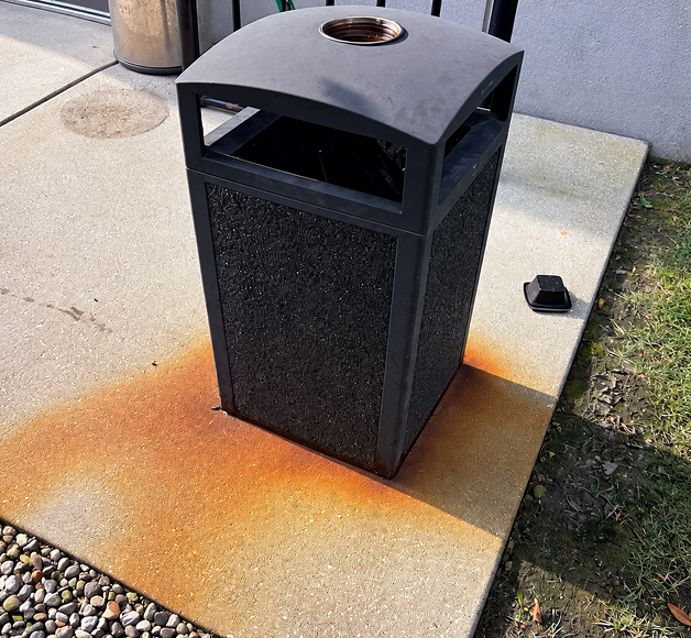 Concrete around a waste bin before cleaning, with heavy rust staining