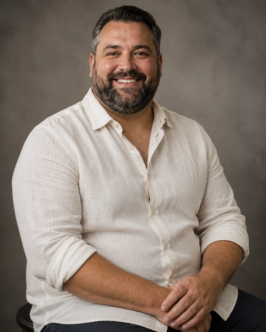 Smiling man in a light linen shirt seated in a photography studio