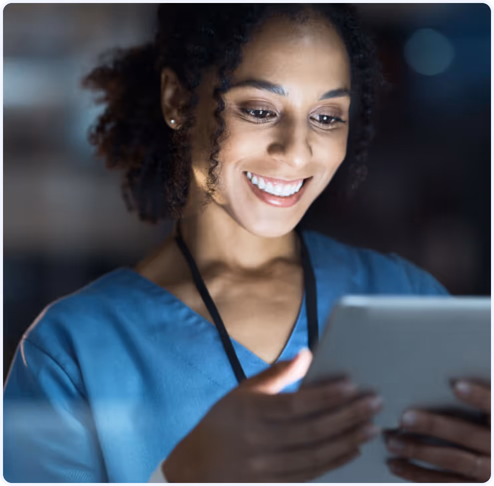 Smiling woman in blue medical scrubs looking at a tablet.