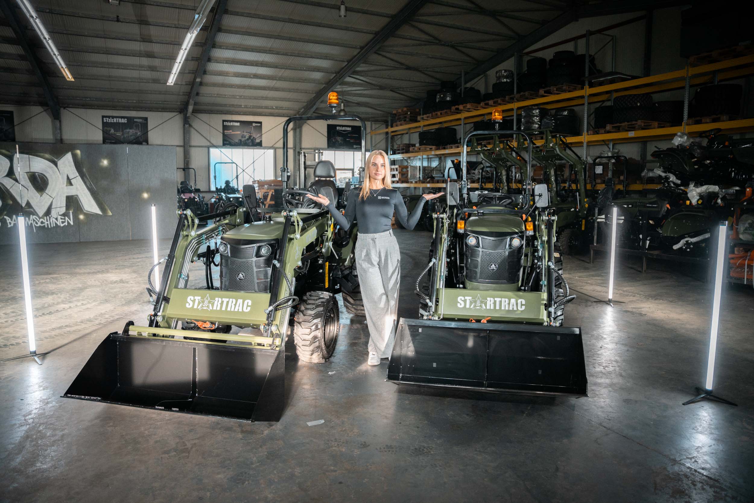 Traktor transportiert im Stall eine große Rundballen-Heuballen, während Kühe in ihren Boxen stehen.