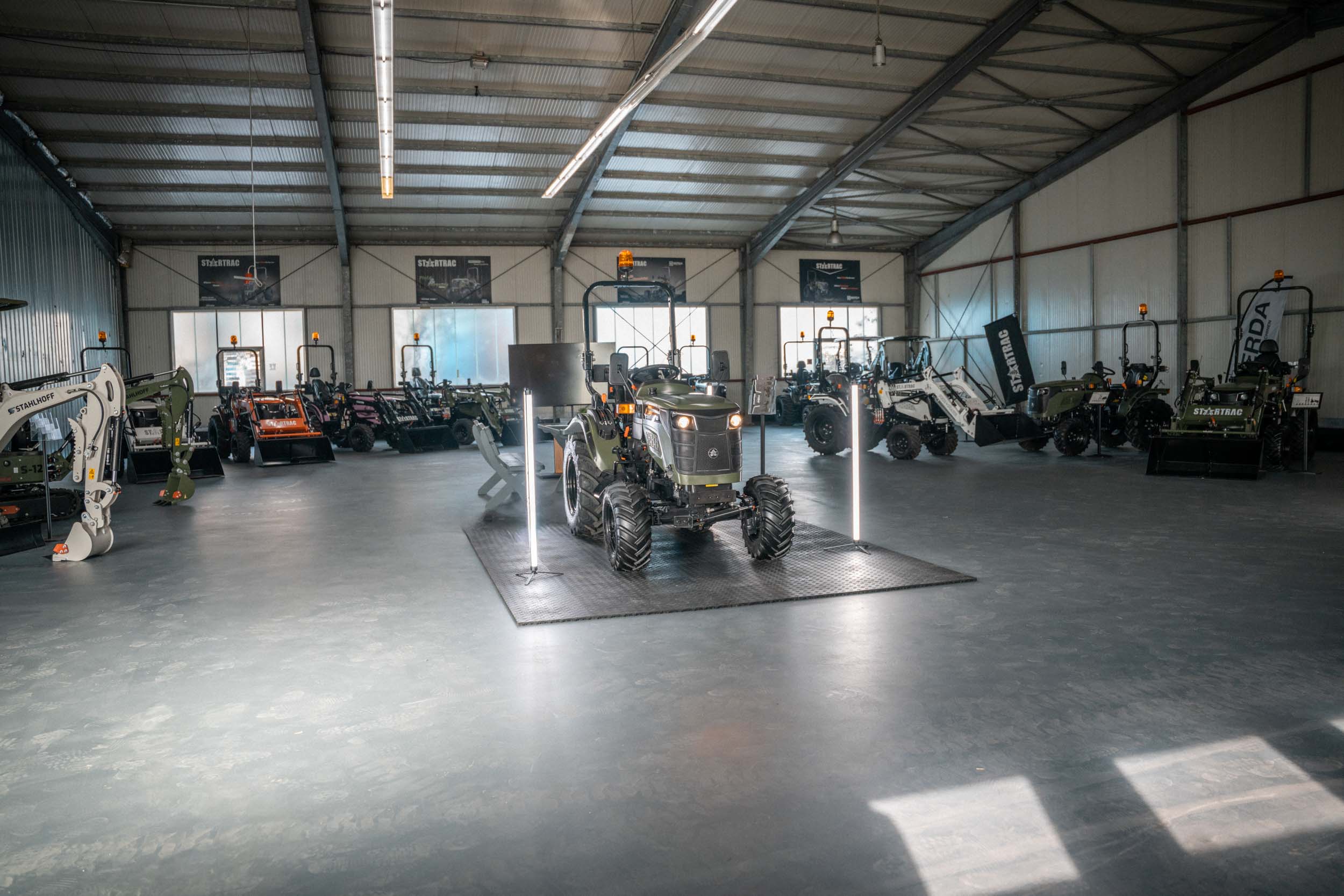 Moderner Traktor mit großen Reifen steht in der Mitte einer Halle, umgeben von weiteren landwirtschaftlichen Maschinen.