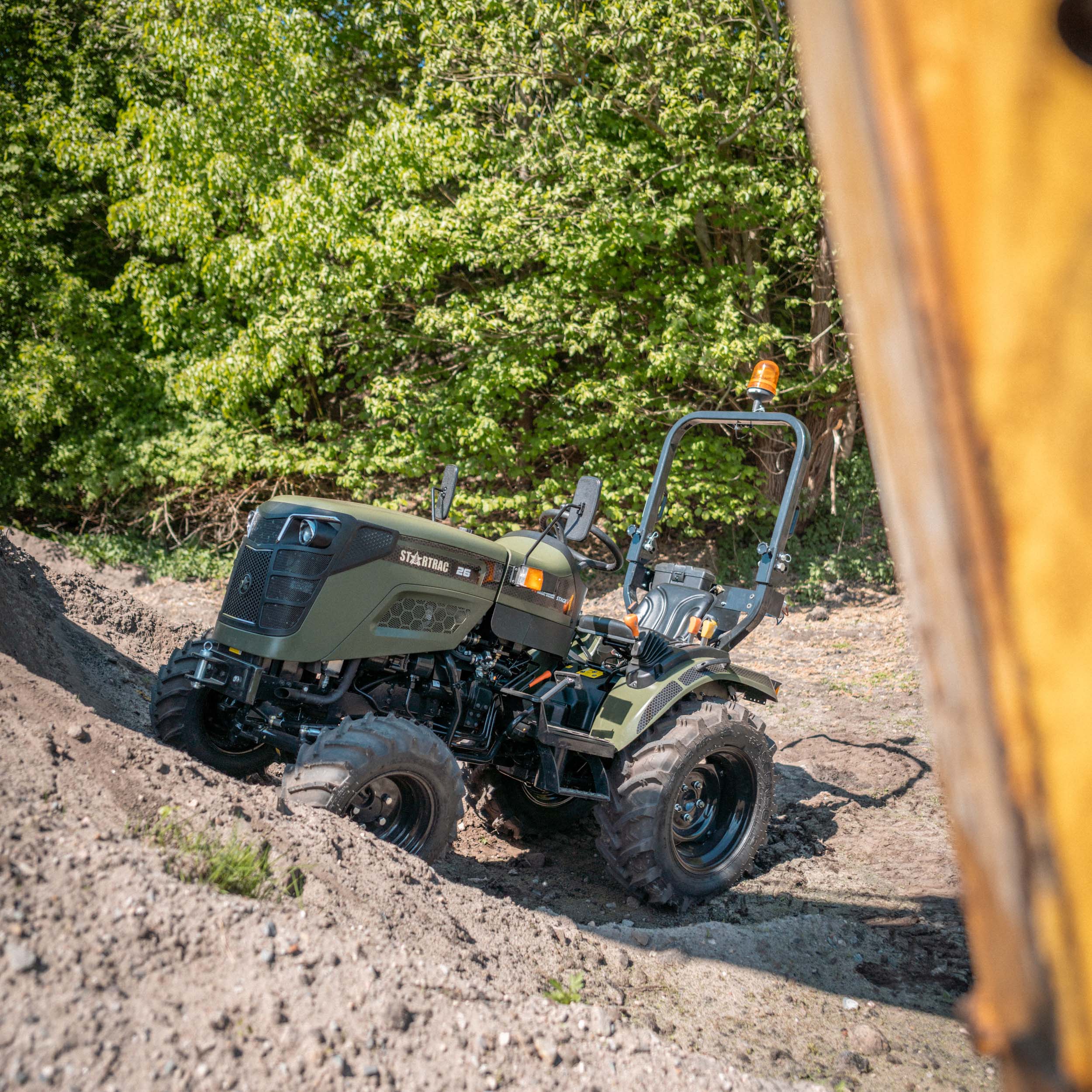 Grüner Startrac 26 Traktor auf unebenem Boden mit Bäumen im Hintergrund.