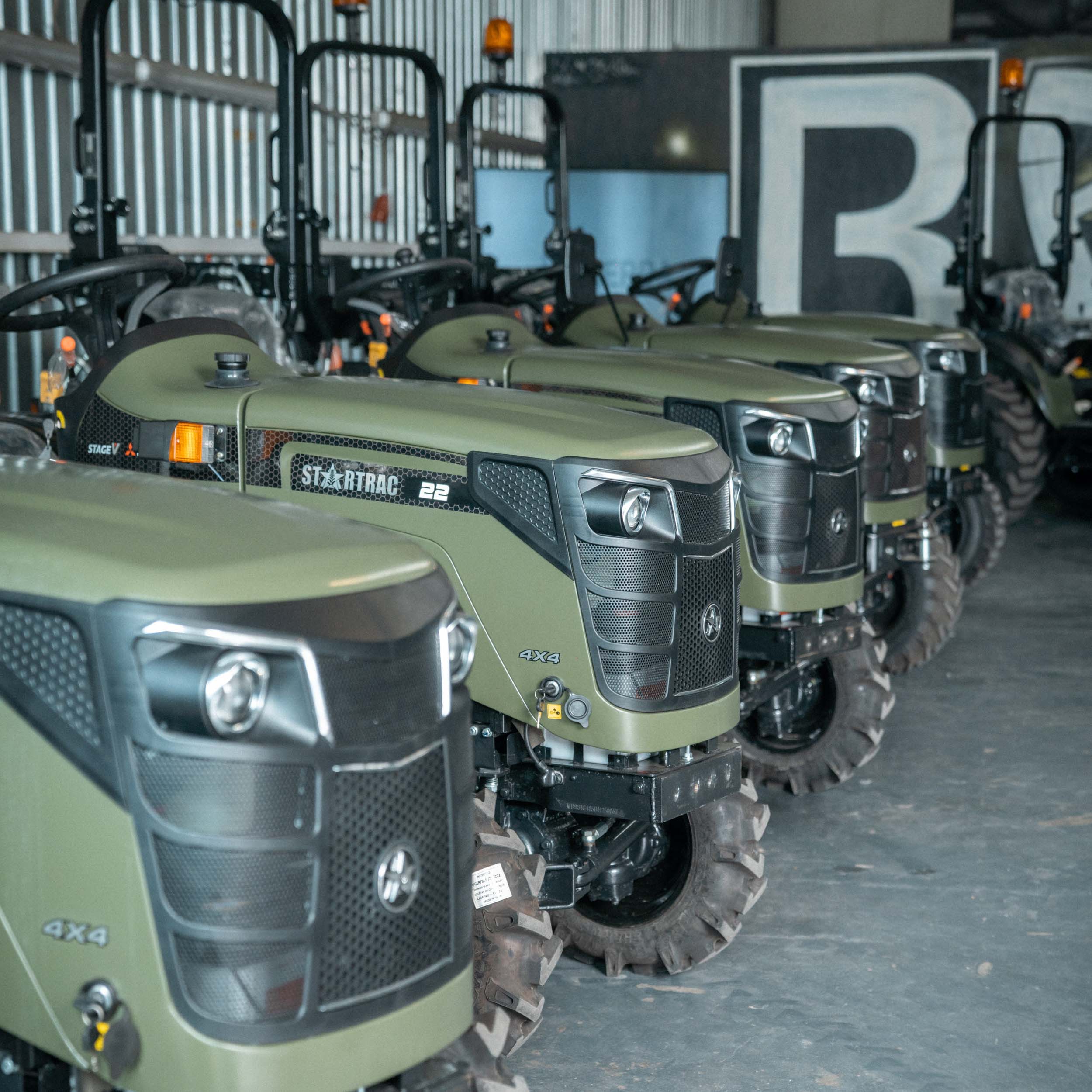 Reihe grüner 4x4 Traktoren vom Modell Startrac 22 in einer Halle geparkt.