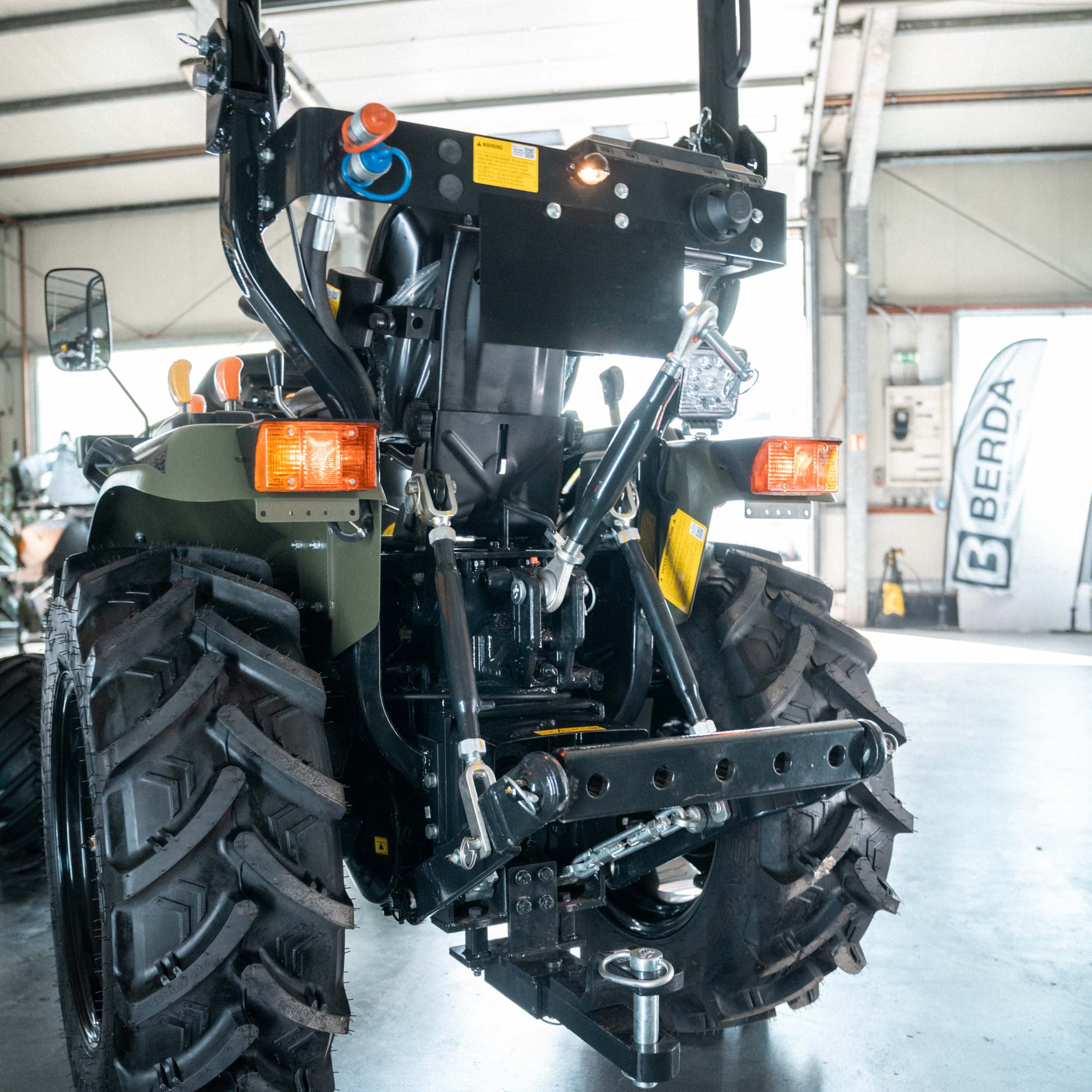 Rückansicht eines grünen Traktors mit großen Reifen in einer Werkstatt mit BERDA-Fahne im Hintergrund.