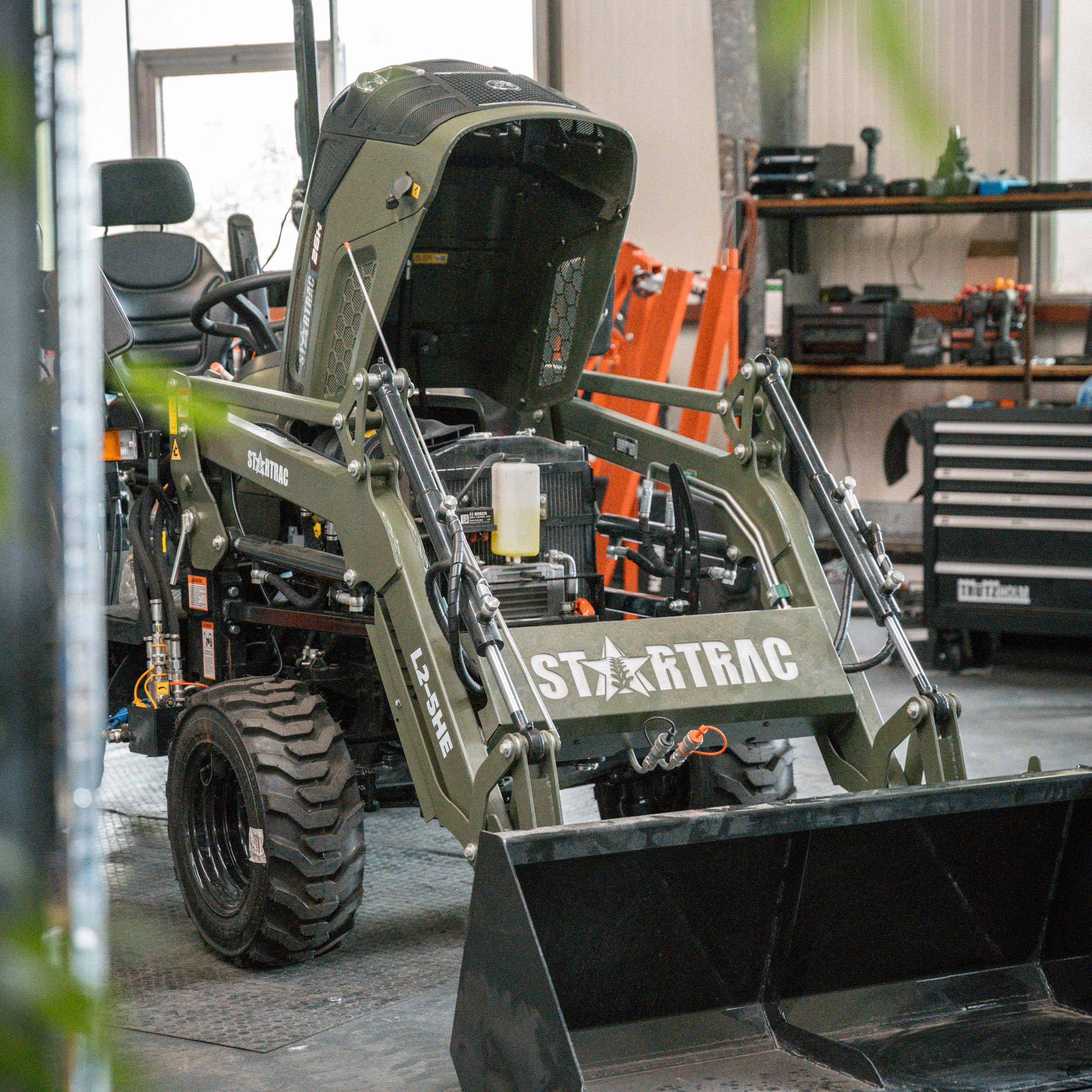 Startrac L2-3HE Minibagger mit hochgeklappter Motorhaube in einer Werkstatt.