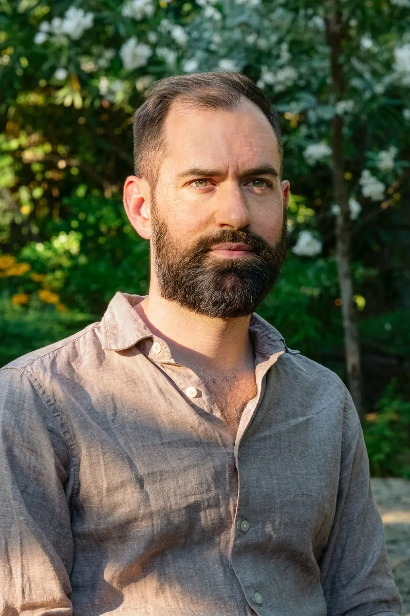 Ignacio Ribera, el fundador de Academia del Paisaje con camisa beige mirando al frente con fondo de árboles y flores blancas al aire libre.
