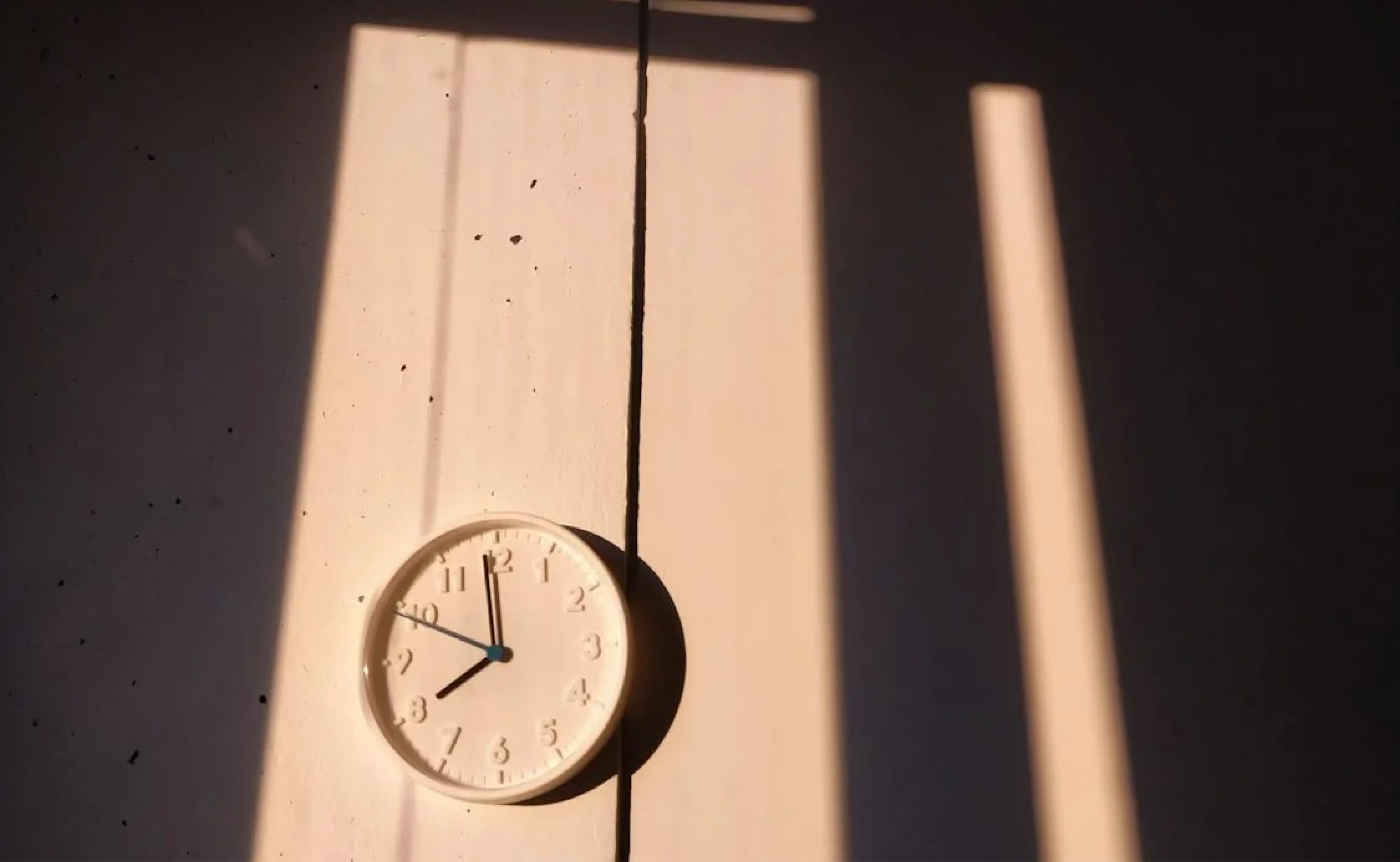 A wall clock with sunlight casting shadows through a window.