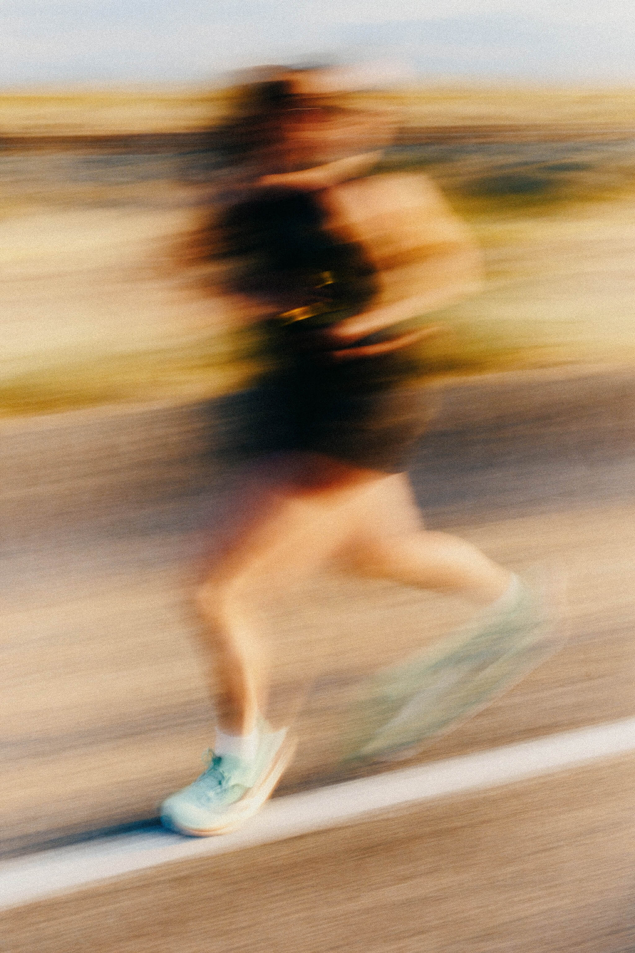 Blurred image of a person running on a road wearing light blue running shoes.