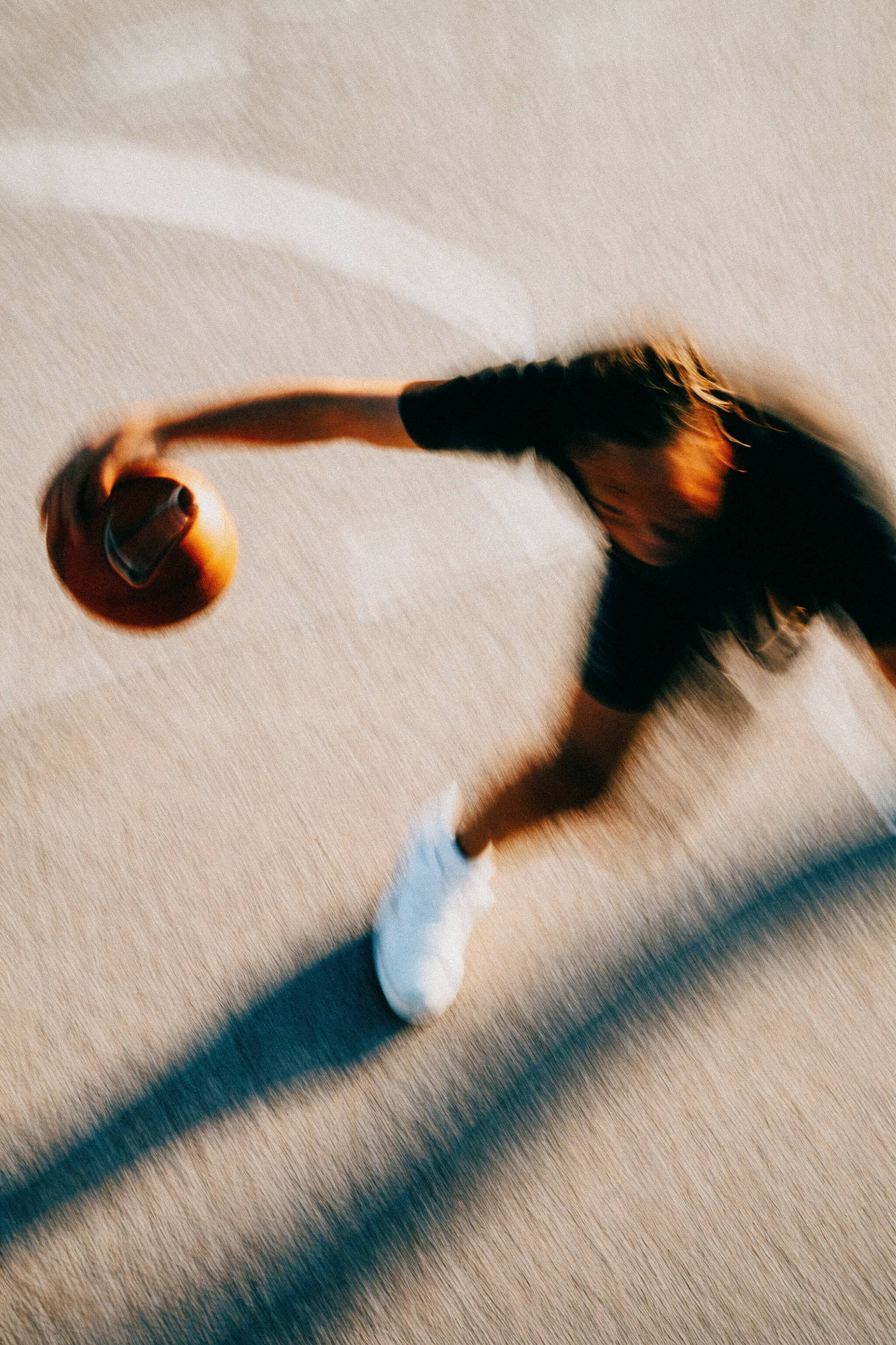 Blurred overhead view of a person in white sneakers holding a basketball on a court.