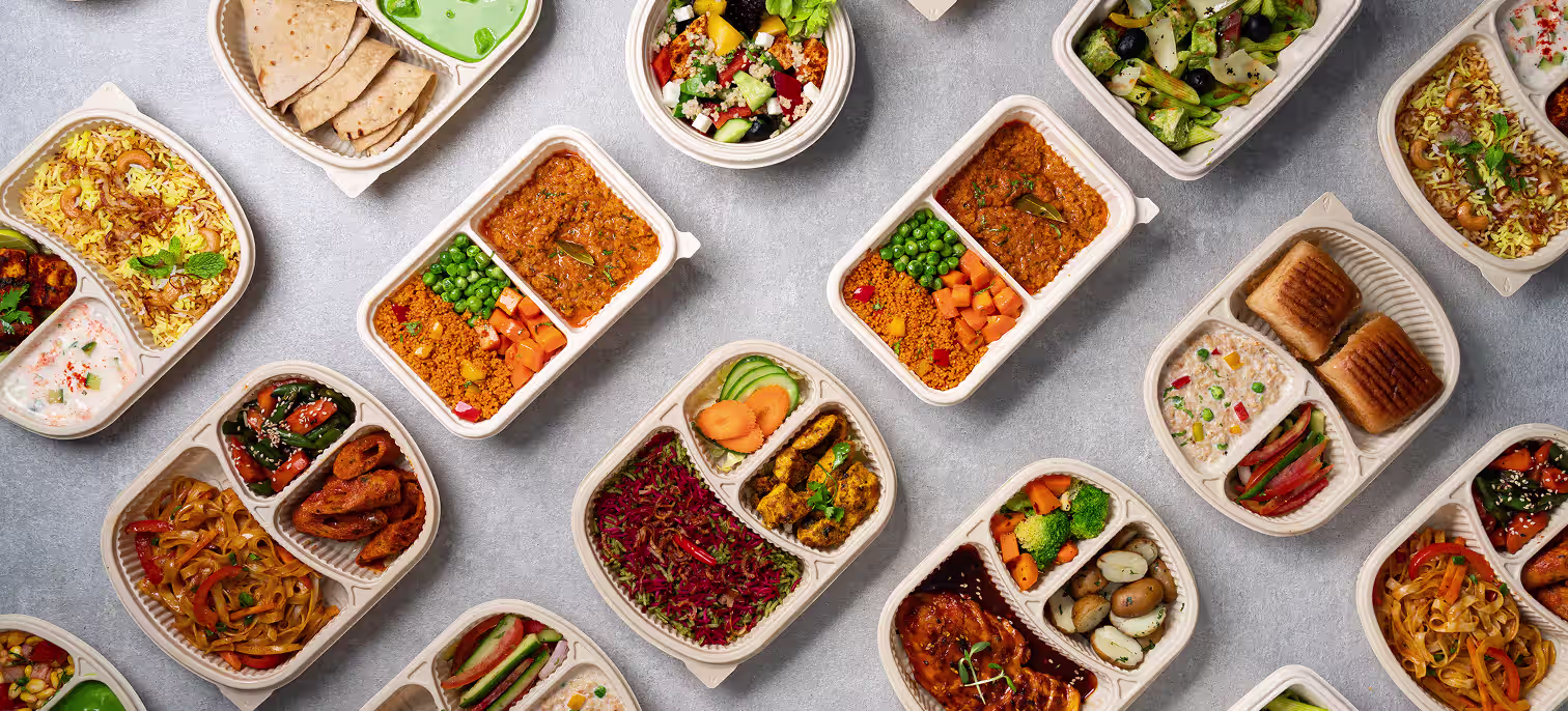 Variety of healthy meal prep containers with rice, vegetables, salads, wraps, and protein dishes on a gray surface.