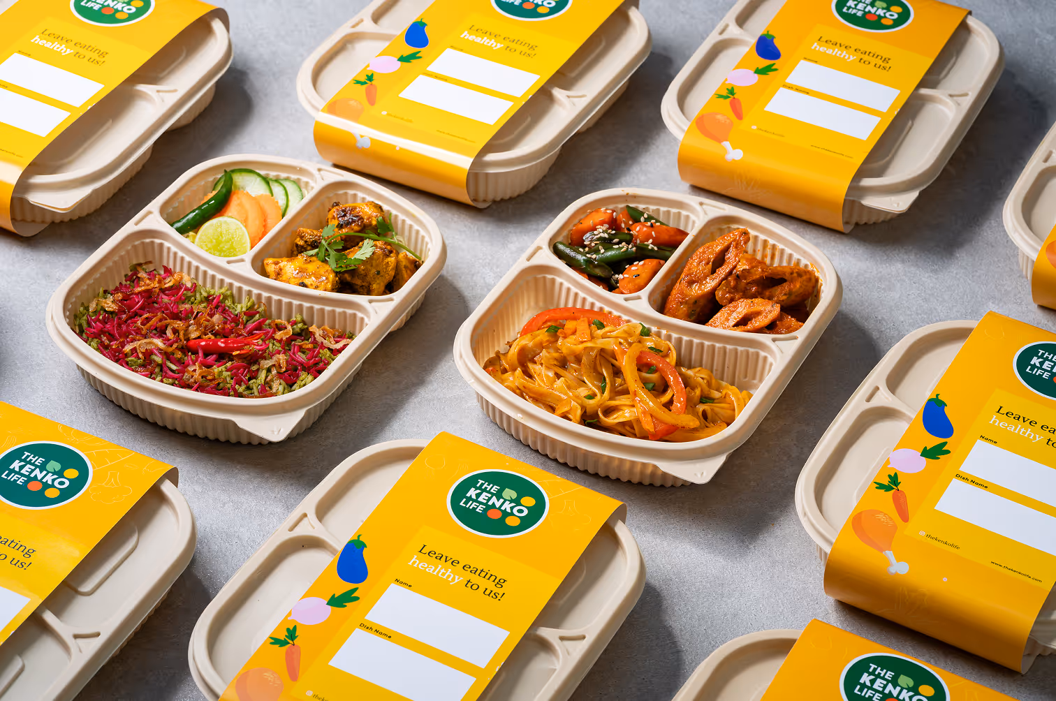 Number of open eco-friendly food containers placed diagonally with healthy meals and yellow branded sleeves from The Kenko Life.