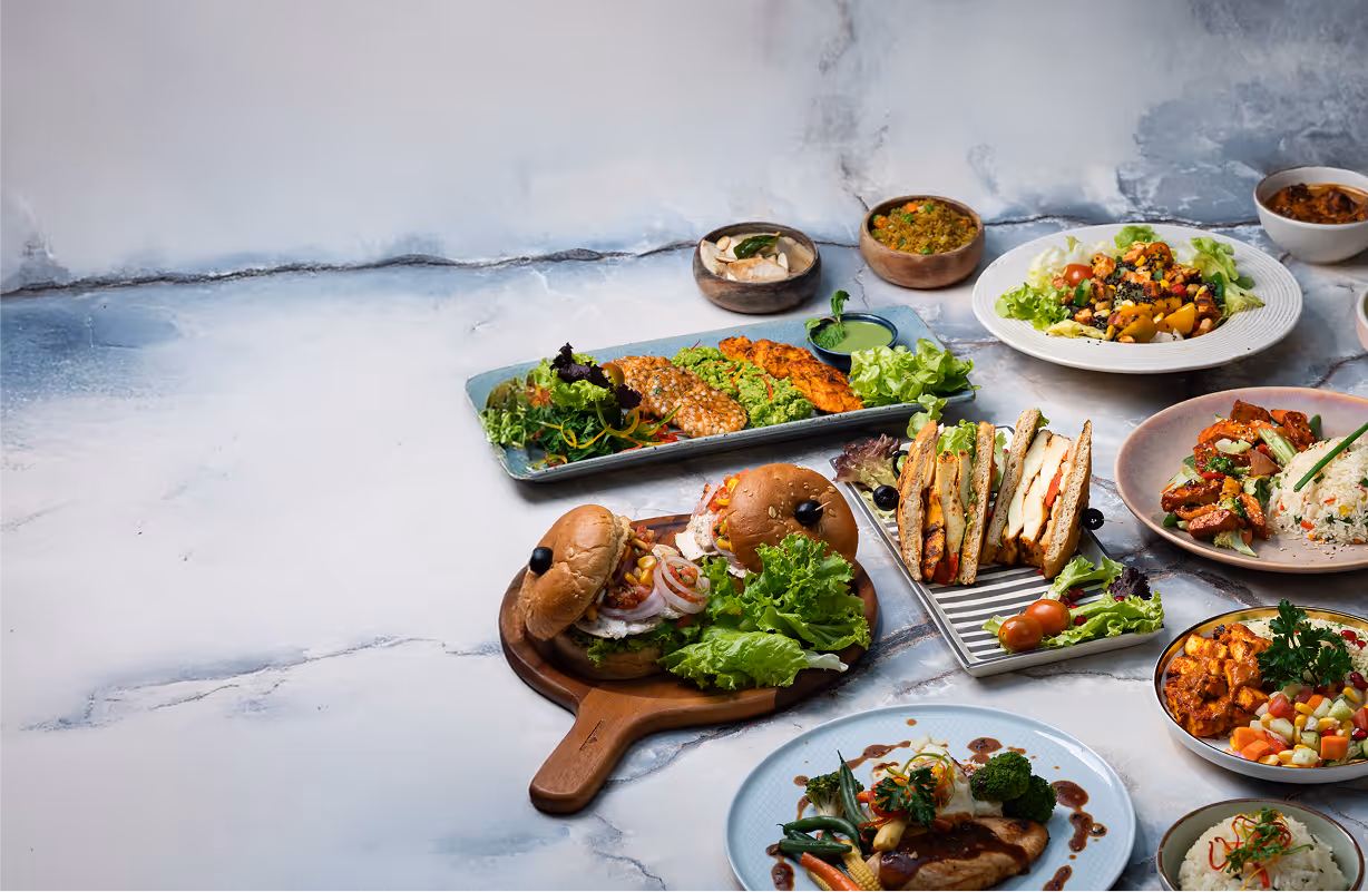 Variety of colorful plated meals including sandwiches, rice dishes, salads, and grilled vegetables on a marble surface.