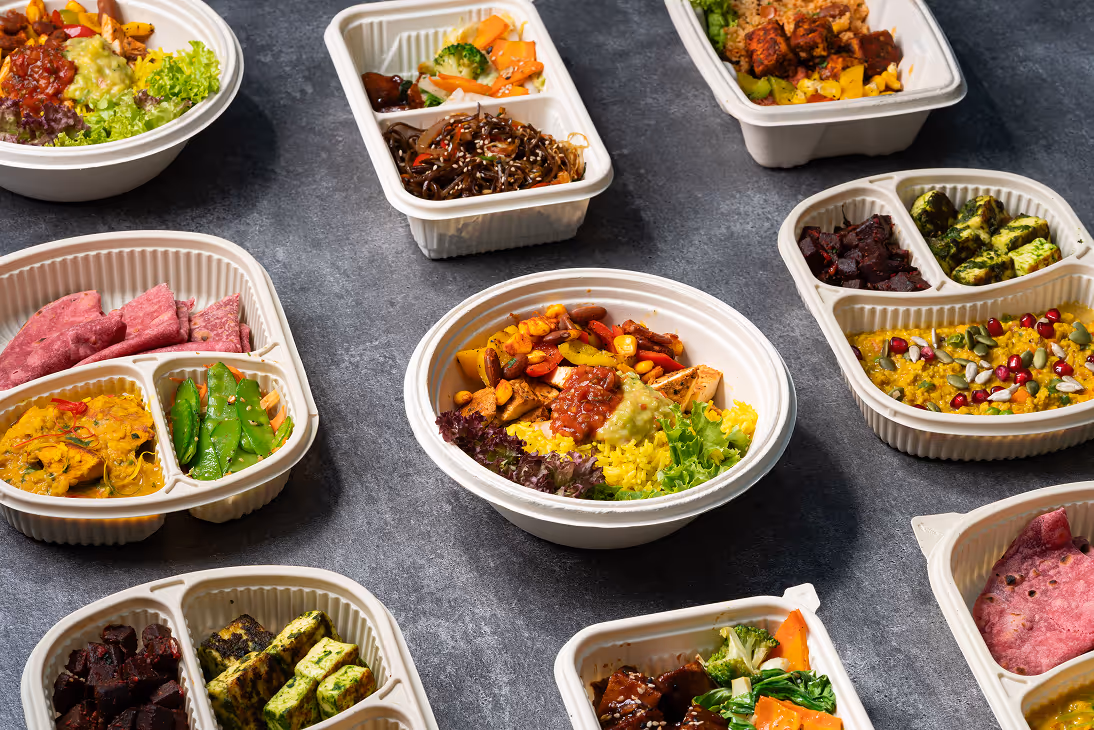 Multiple meal prep containers with colorful healthy foods like rice, beans, vegetables, and greens on gray surface.