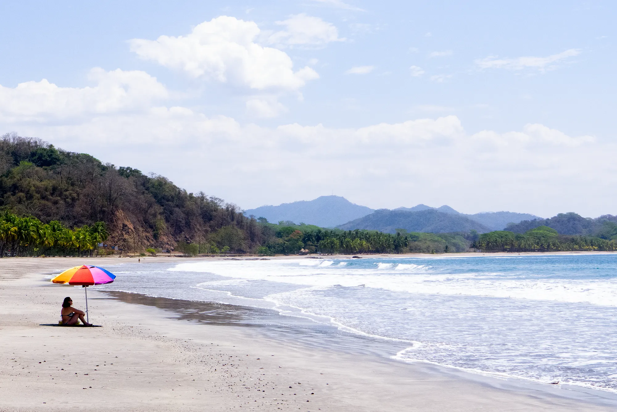 A Pacific beach backed by green mountains with a colorful umbrella on the sand in Costa Rica