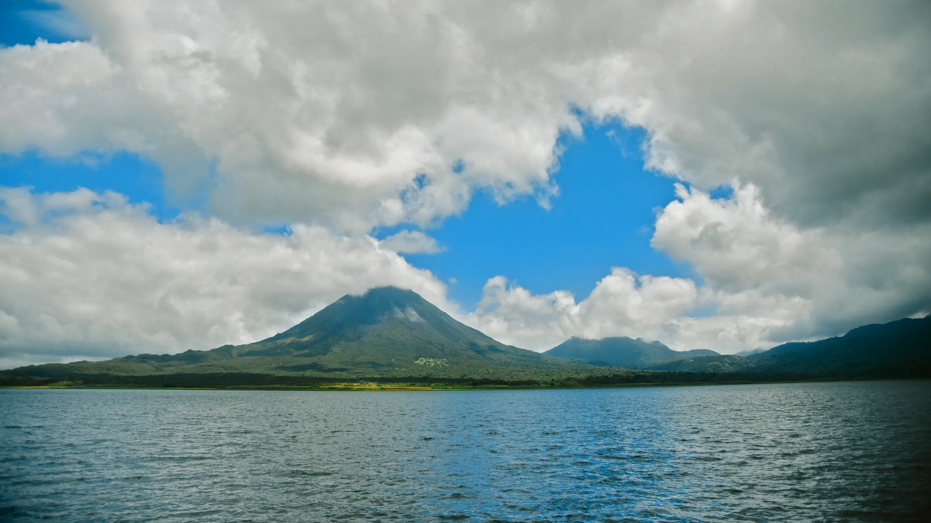 Arenal Volcano rising under a blue, cloud-filled sky in Costa Rica
