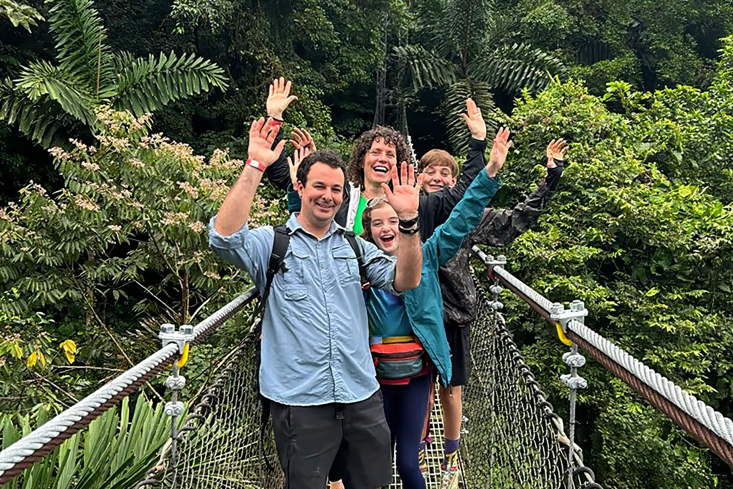 A family waving from a hanging bridge in the rainforest canopy in Costa Rica