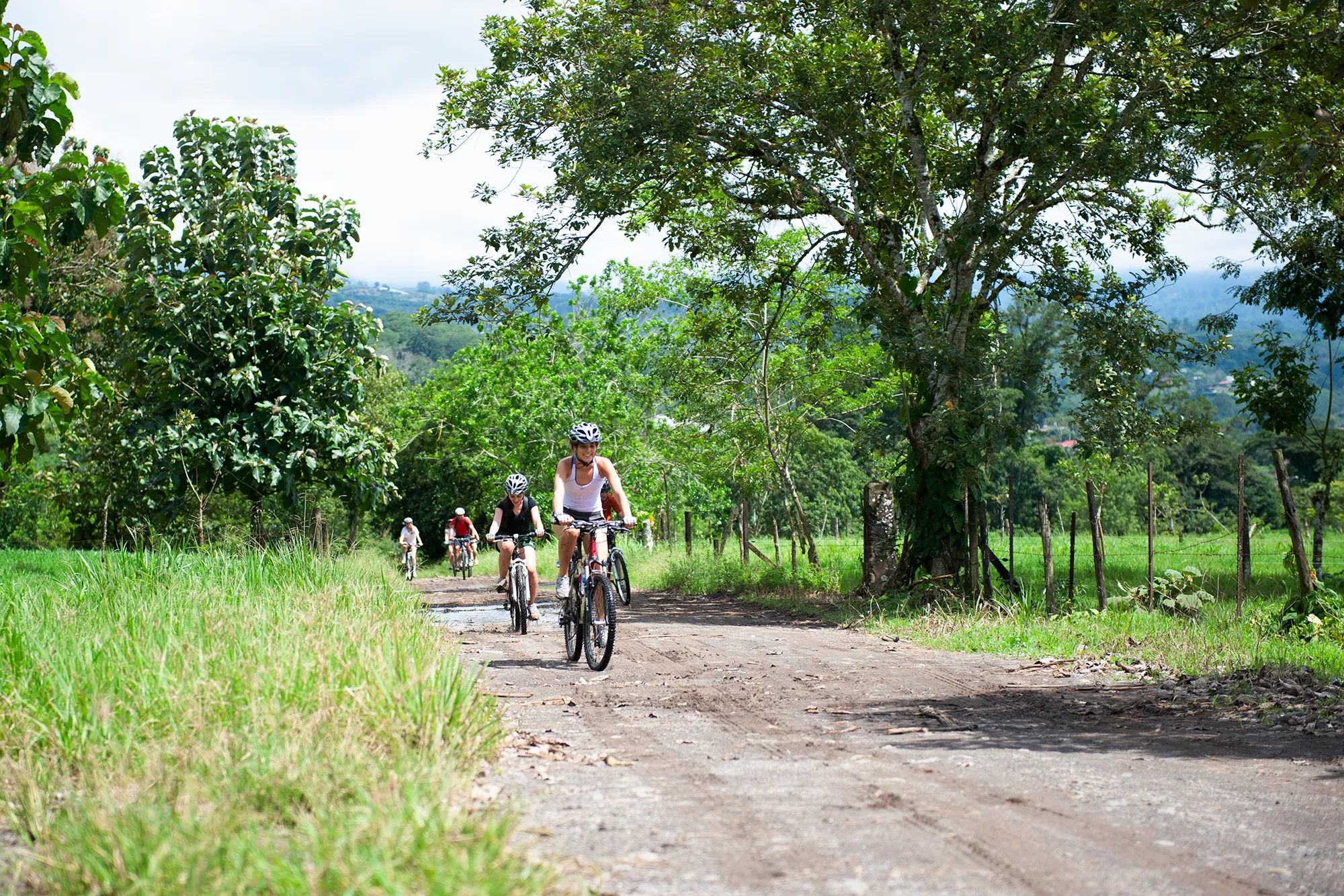 A group mountain biking along a dirt road through green countryside in Costa Rica