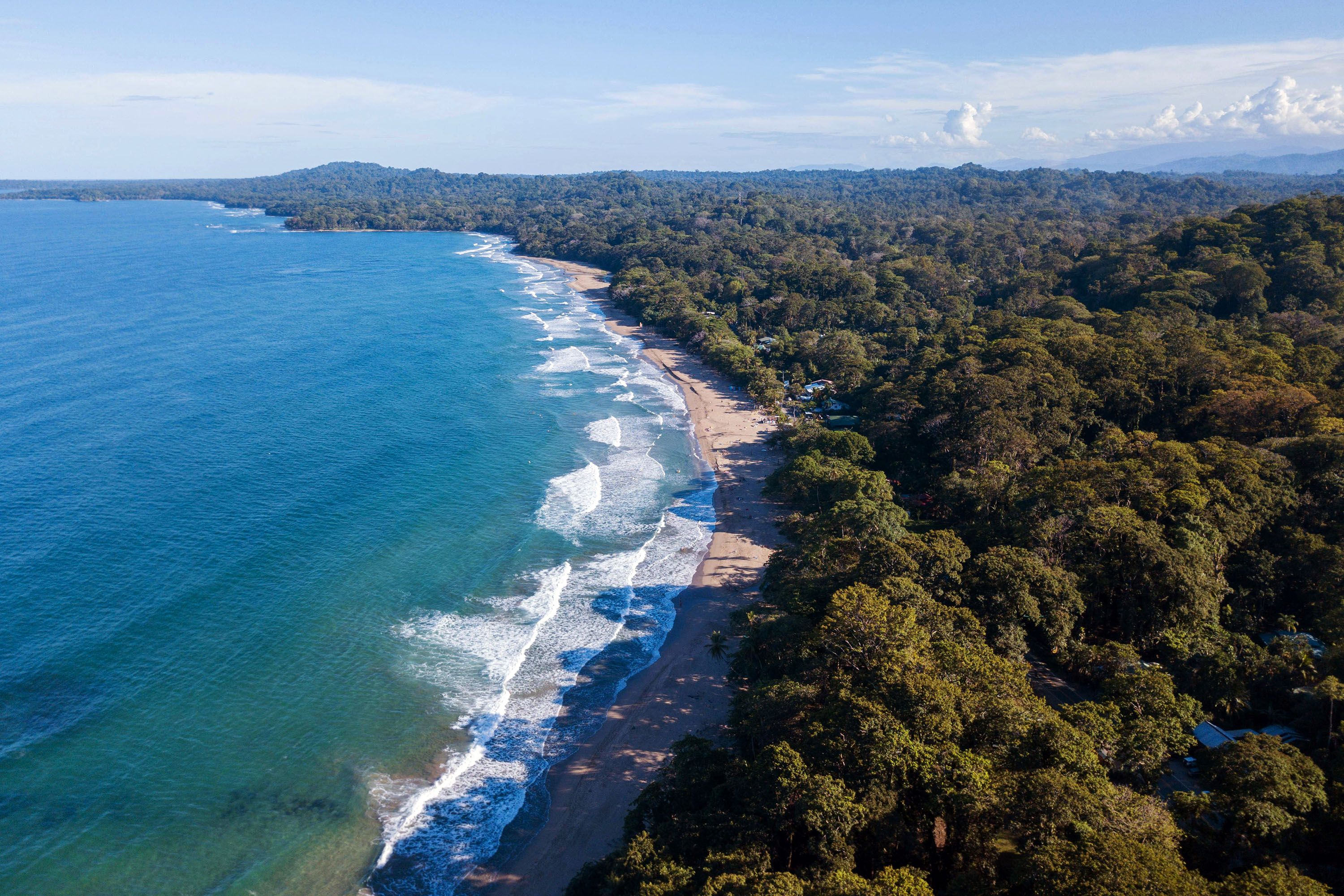 An aerial view of forested coastline meeting a dark-sand beach in Costa Rica