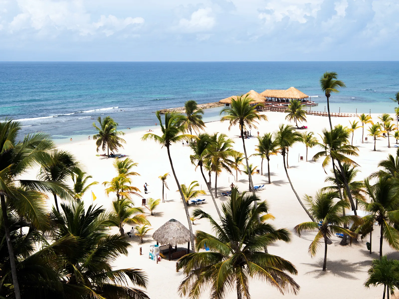 A resort beach lined with palm trees and a pier over turquoise water in the Dominican Republic