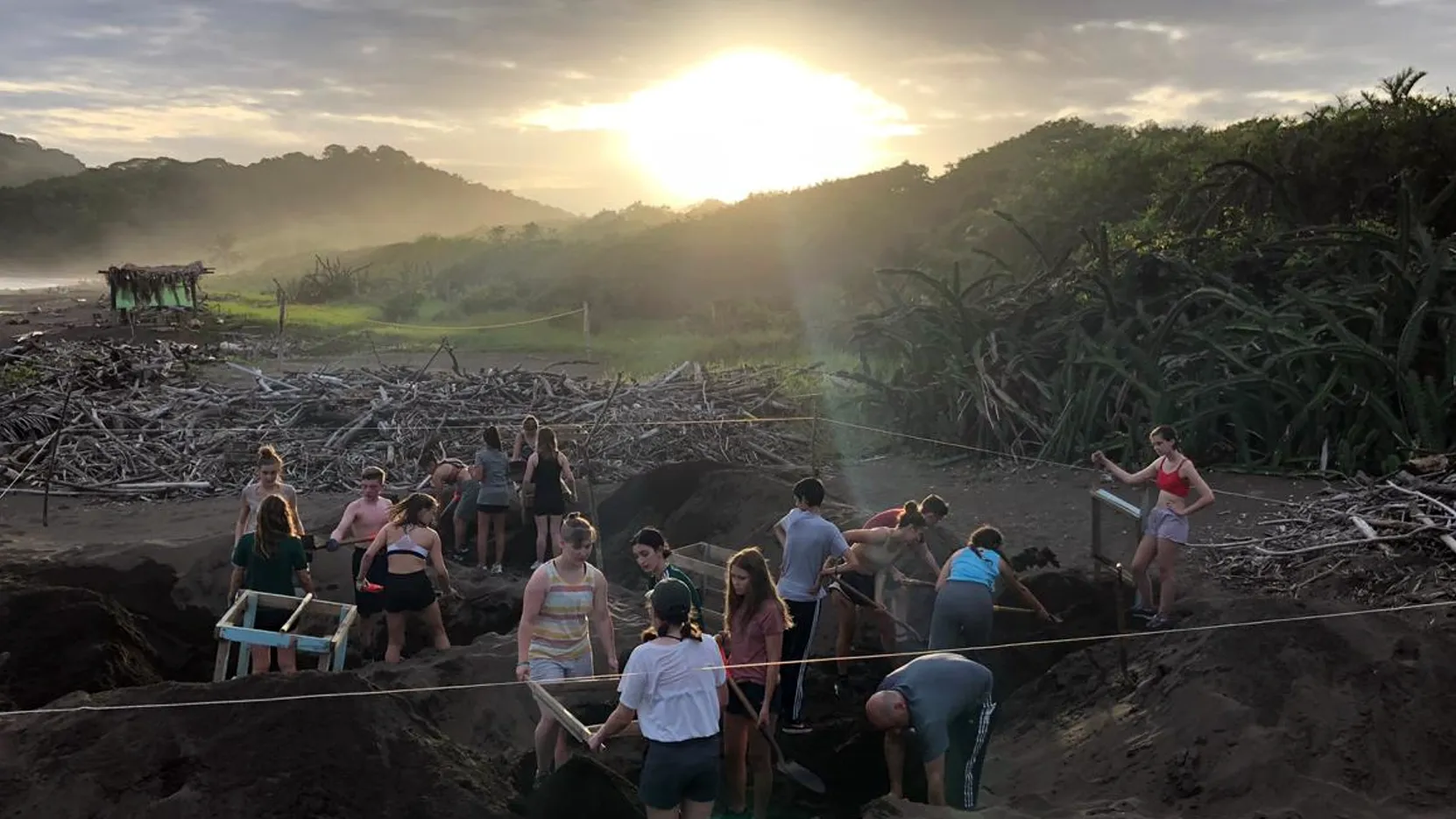 A group of students gathered on a dark-sand beach at dawn during a sea turtle conservation project in Costa Rica