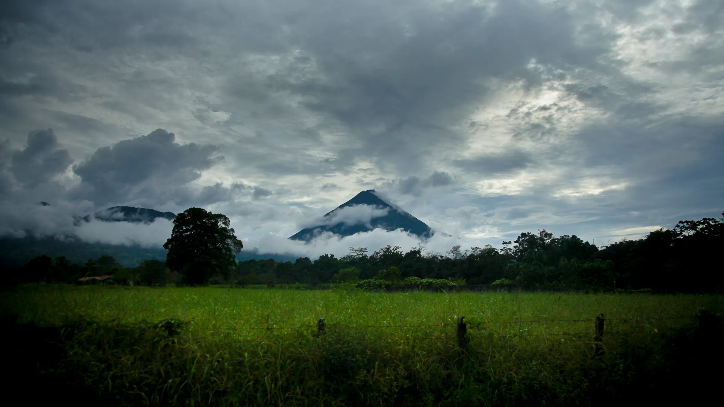 Arenal Volcano wreathed in clouds rising over green fields in Costa Rica