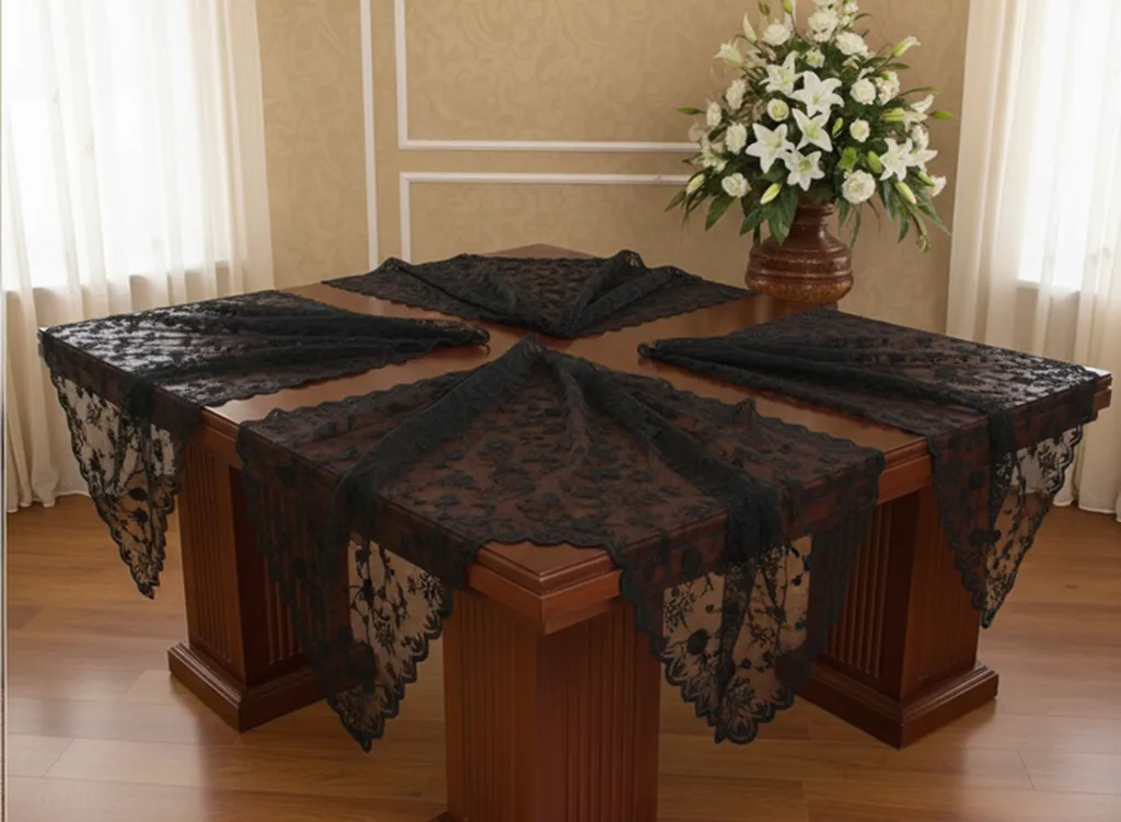Četvrtasti drveni sto sa crnim čipkastim stolnjacima na svakoj strani i vaza sa belim ljiljanima na stolu.