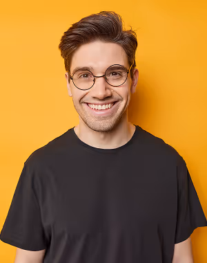 Young man wearing round glasses and a black t-shirt smiling against a bright orange background.