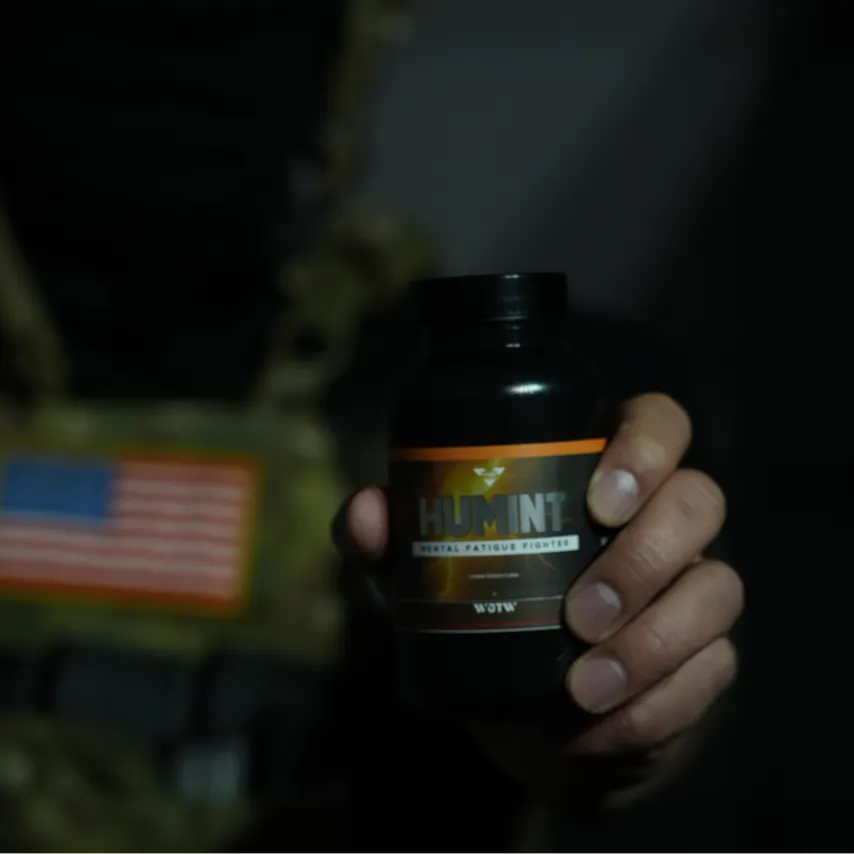Hand holding a black bottle labeled HUMINT Mental Fatigue Fighter against a dark background.