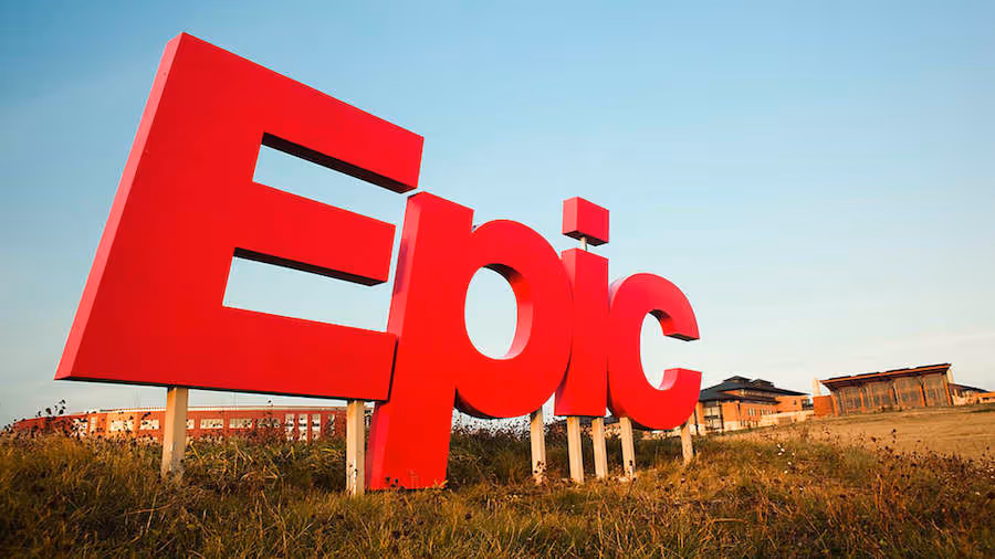 Large red 3D letters spelling 'Epic' standing outdoors on grass with buildings in the background under a blue sky.