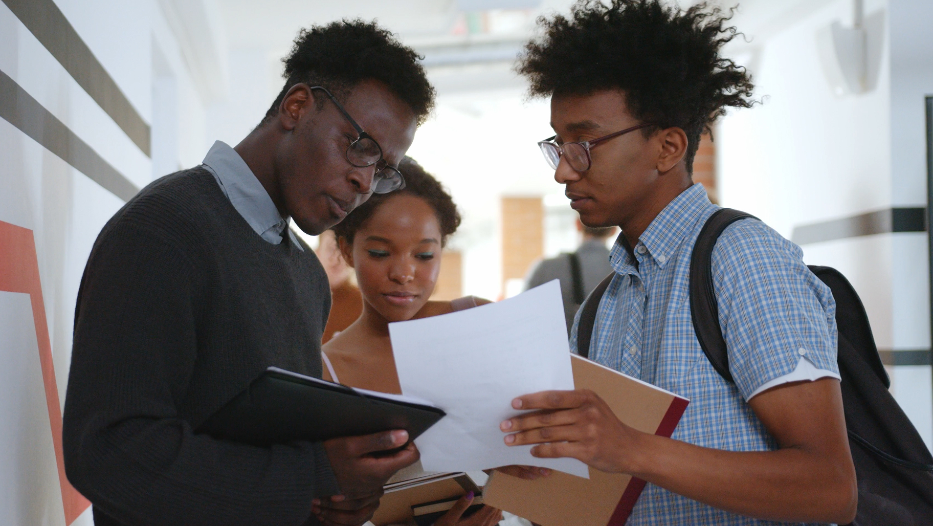 Trois étudiants examinent un document ensemble dans un couloir universitaire