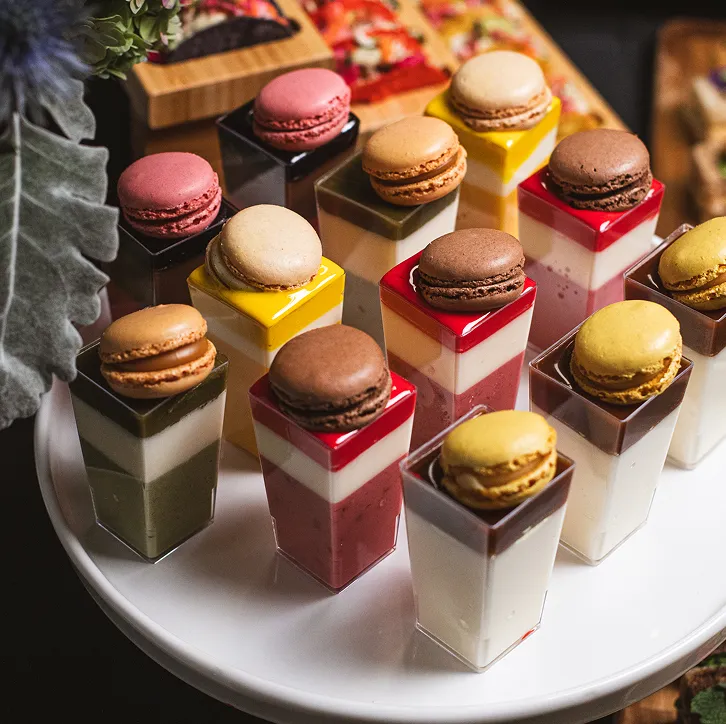 Macarons atop layered mousse dessert cups on a white cake stand