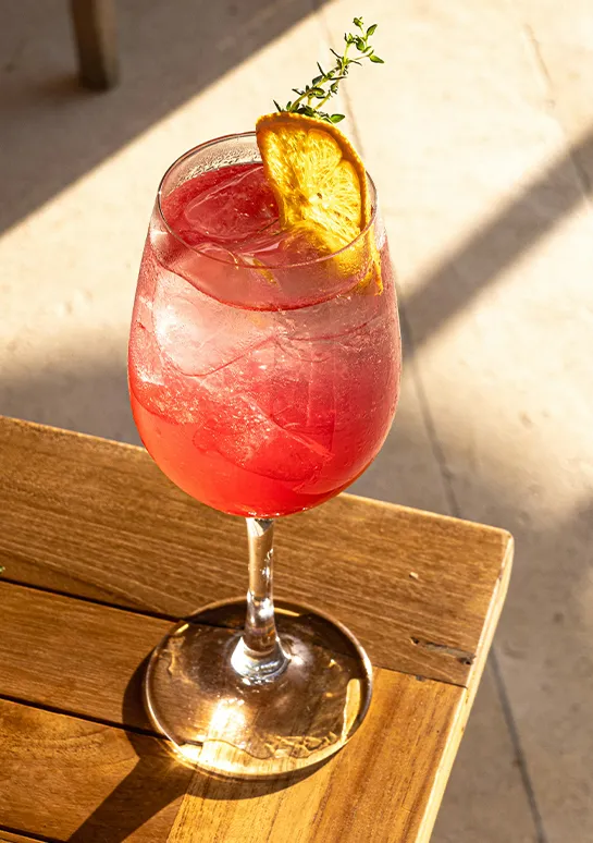 Pink spritz cocktail garnished with a dried orange slice and thyme