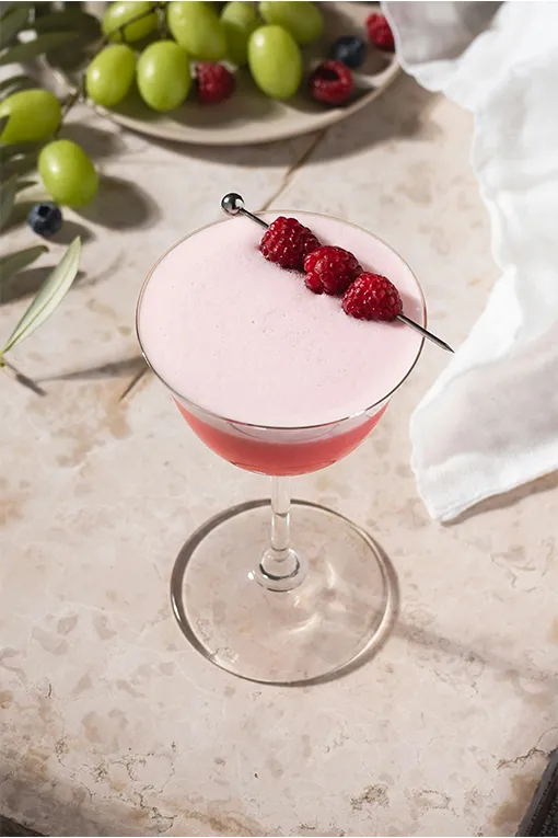 Pink foam-topped cocktail in a coupe glass garnished with skewered raspberries