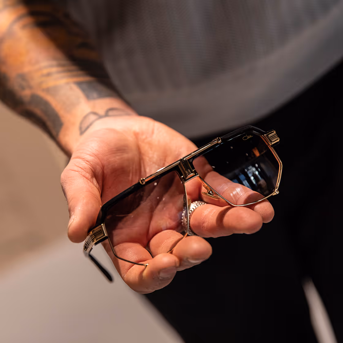 hand holding sunglasses with dark angular lenses and gold frames.