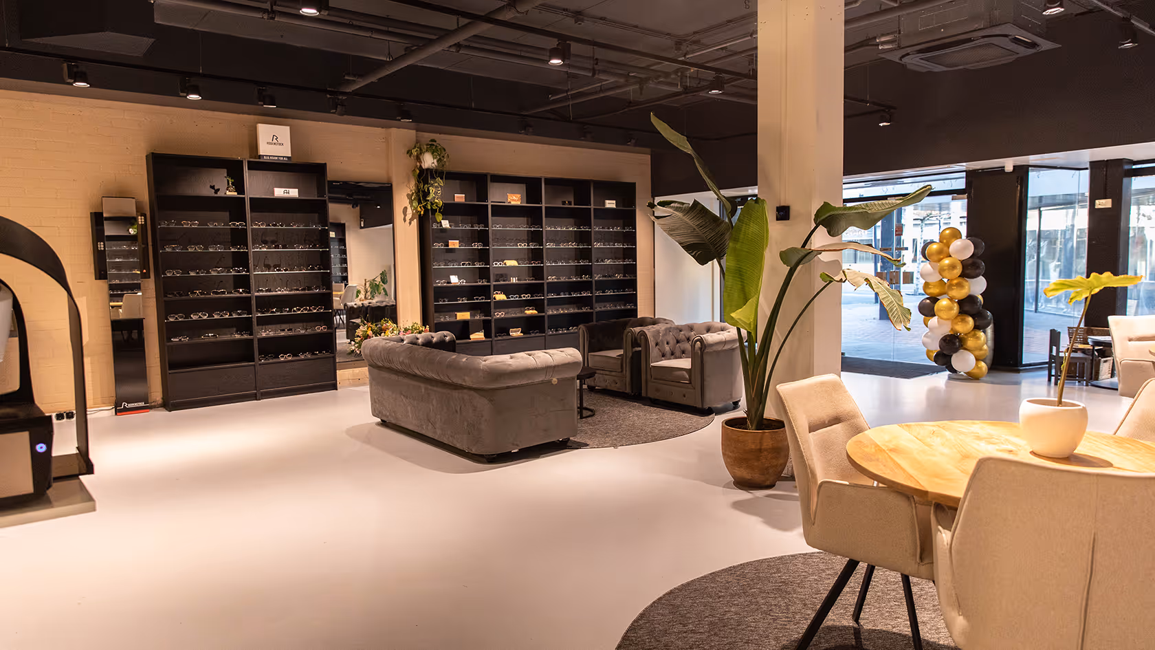 Modern eyewear store interior with shelves of glasses, grey sofas, round tables, and green potted plants.