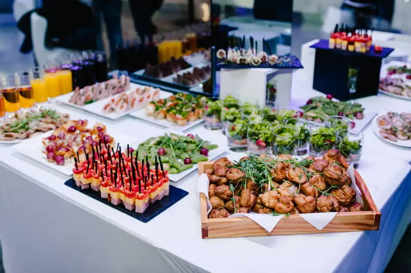Mesa con variedad de aperitivos y cócteles, incluyendo canapés, brochetas, ensaladas en vasos y zumos en vaso de cristal.