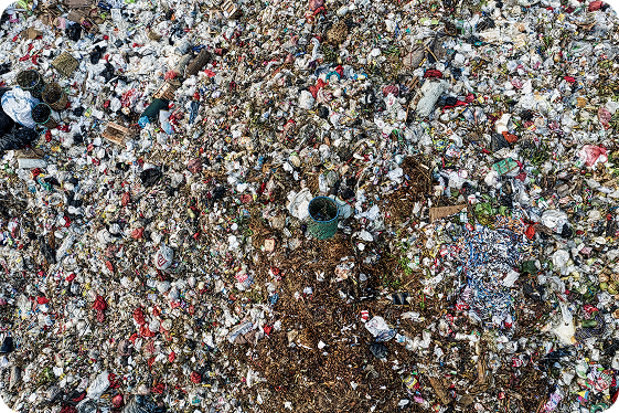 Aerial view of a large pile of mixed garbage including plastic bags, containers, and organic waste scattered over a wide area.