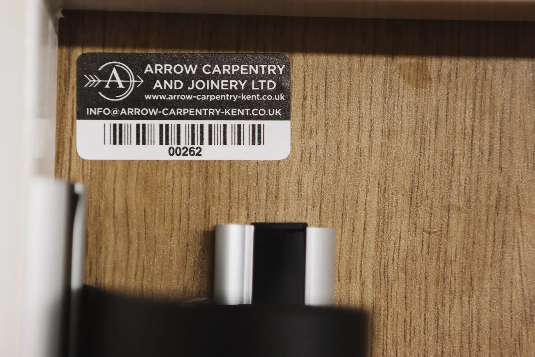 Close-up of a barcode label from Arrow Carpentry and Joinery Ltd attached to a wood surface.