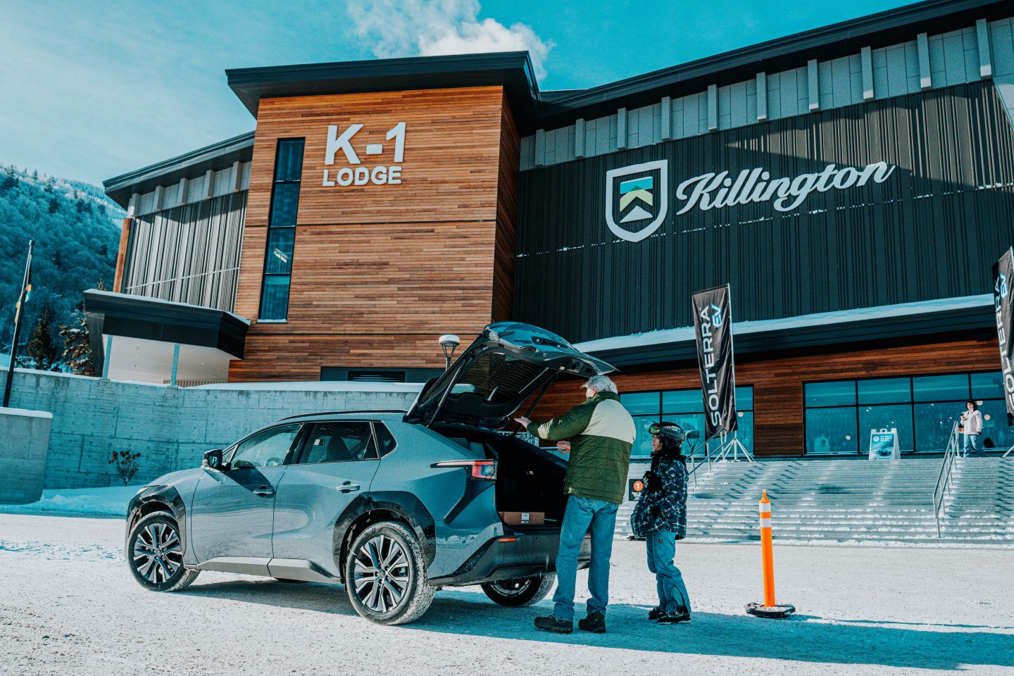 Man and child loading a gray SUV parked on snow in front of K-1 Lodge at Killington ski resort.
