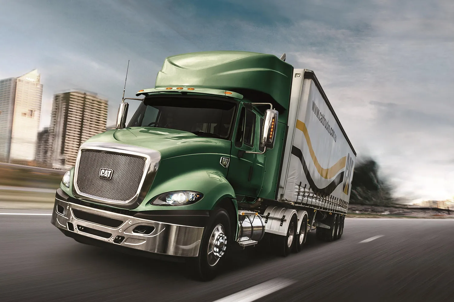 Green CAT semi-truck driving on a highway near a city with tall buildings.