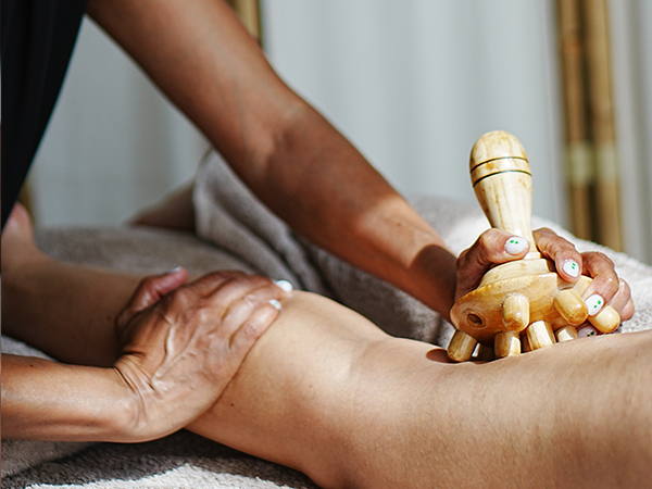 Een persoon krijgt een beenmassage met een houten massageroller.