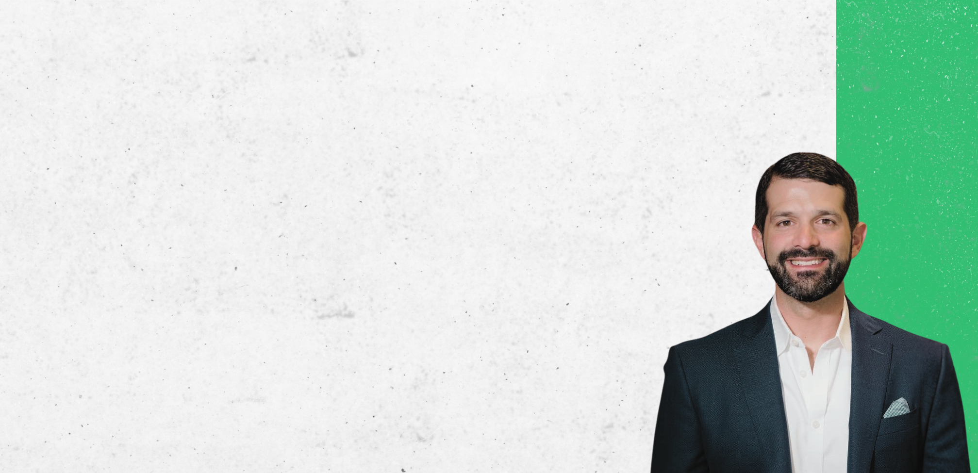 Zack Gould headshot. Smiling man with dark hair and beard wearing a dark suit jacket and white shirt standing against a white and green background.