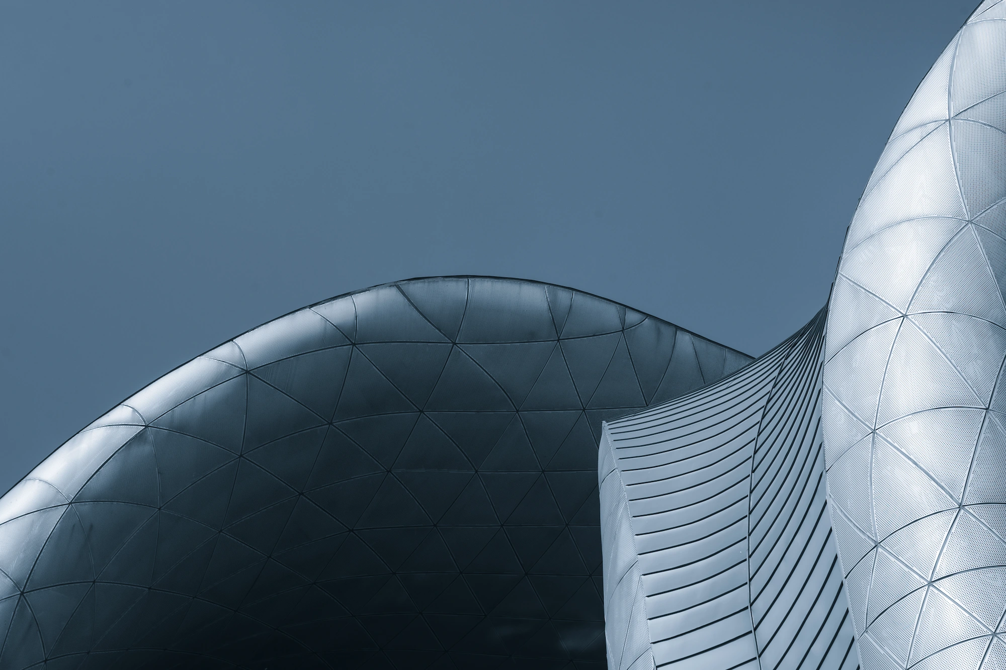 Close-up of futuristic curved metallic architecture panels under a clear blue sky.