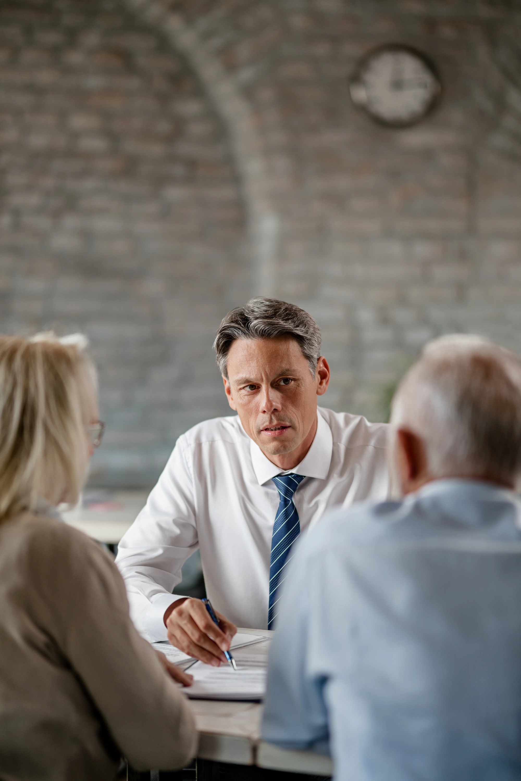 Financial advisor in white shirt and blue tie discussing documents with an elderly couple in an office.