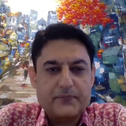 Man with short black hair wearing a red patterned shirt in front of a colorful cityscape painting.